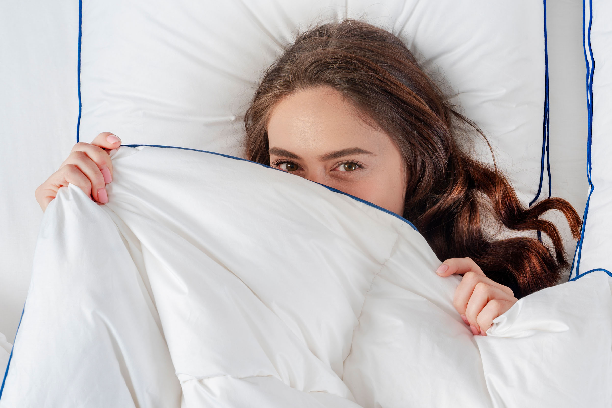 Girl laying under white down duvet on a white bed