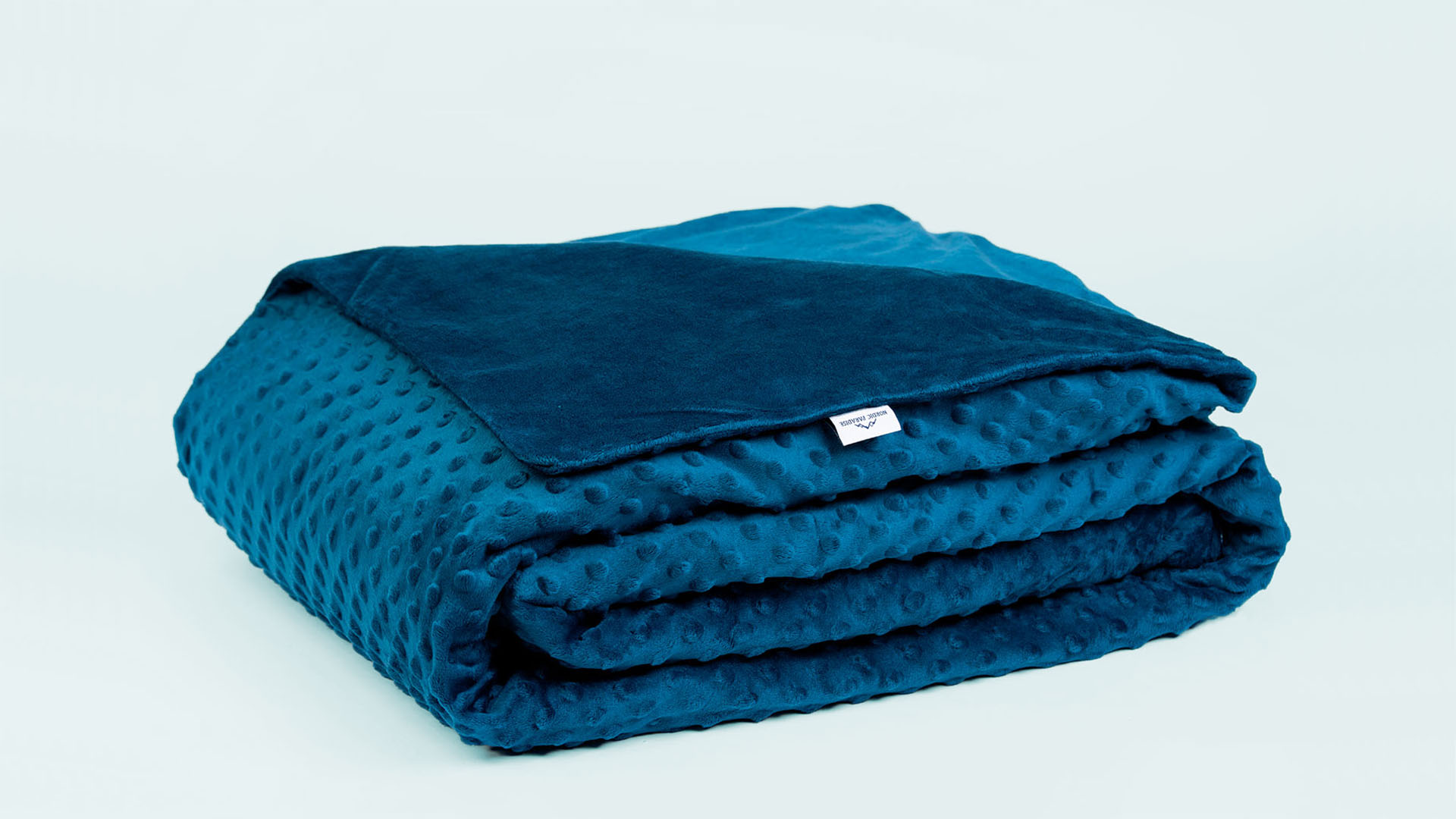 Side view of folded blue weighted blanket with a minky dotted cover on blue background