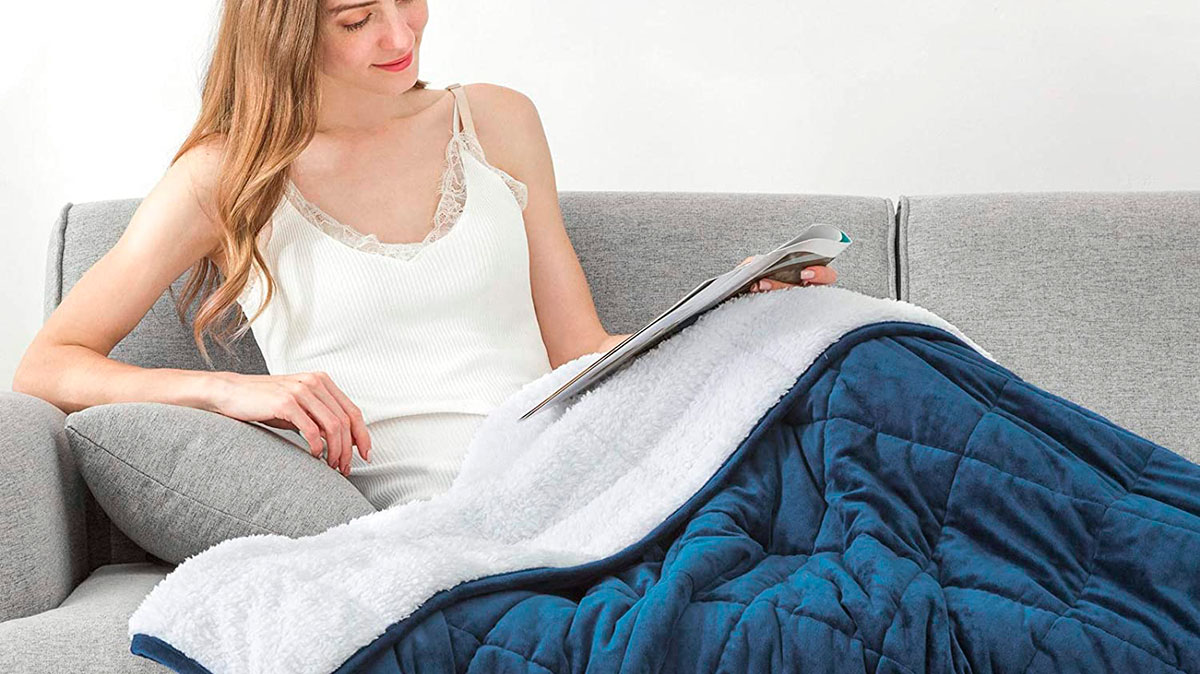 Girl sitting on a sofa and reading a magazine covered with blue and white weighted blanket