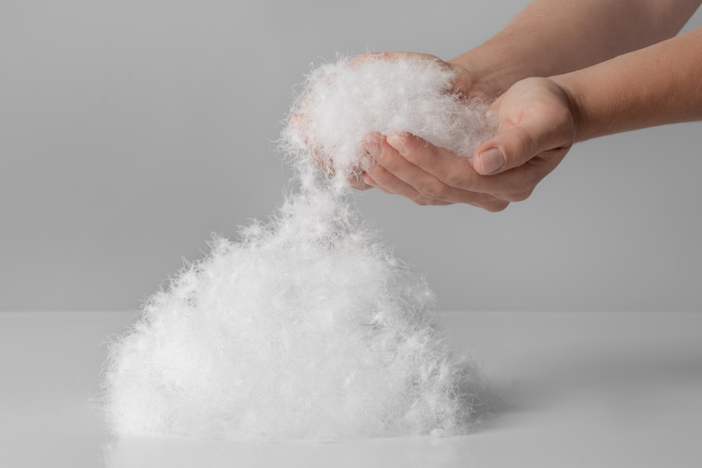 Hands holding a cluster of down from a pile of down clusters